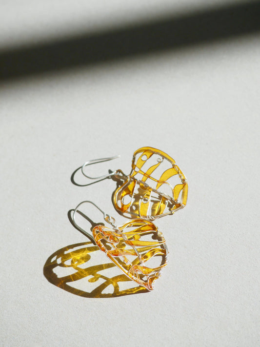 Two leaf shaped earrings in light amber color on a grey background 
