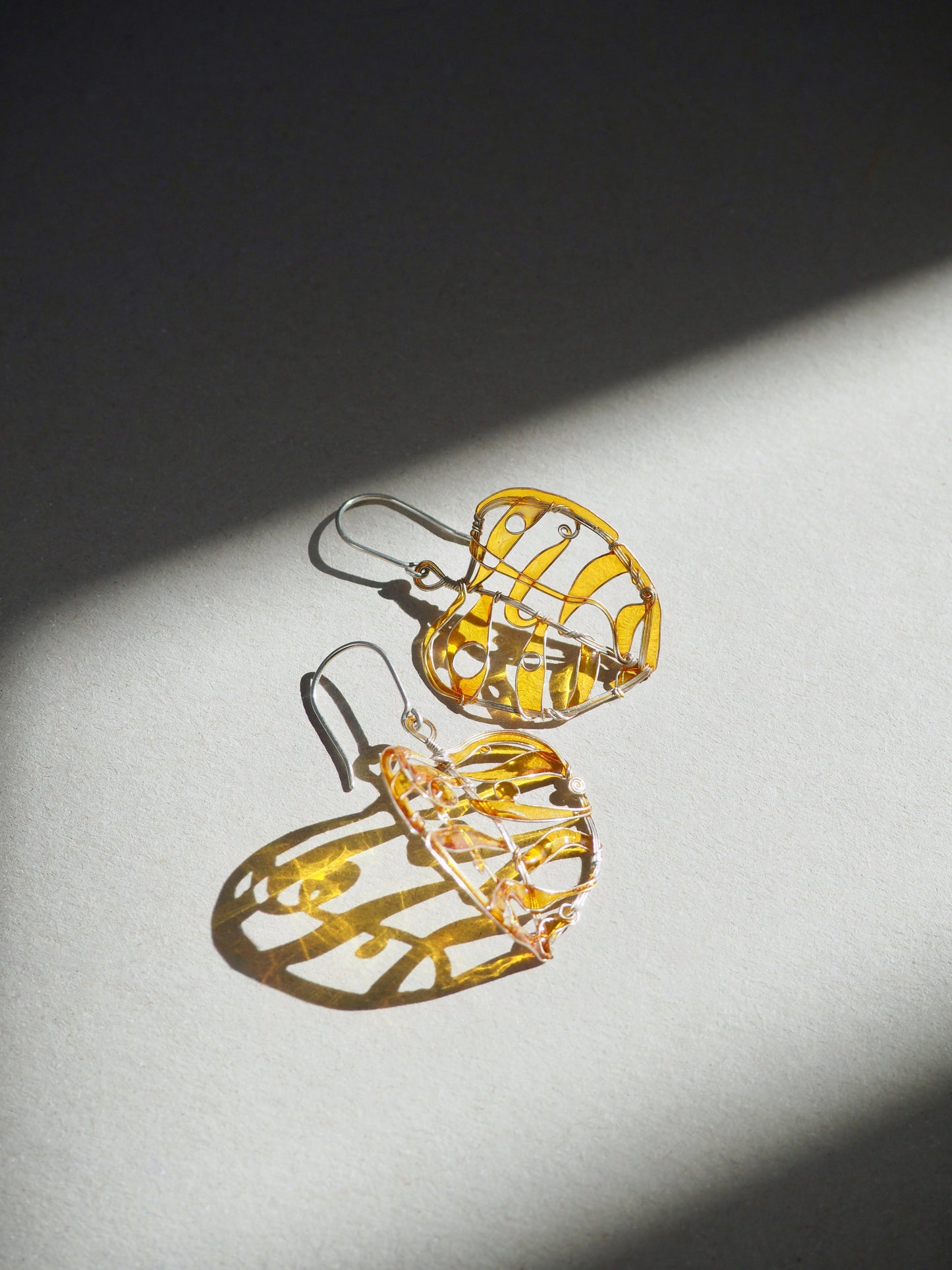 Pair of silver earrings in yellow to orange color on a grey surface with a dark shadow