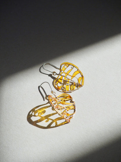 Pair of silver earrings in yellow to orange color on a grey surface with a dark shadow