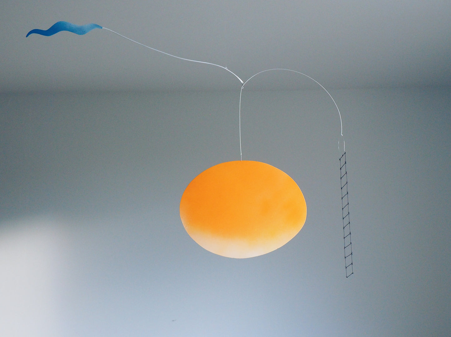 A metal sculpture featuring an orange circle element, a blue cloud and a black metal ladder. 