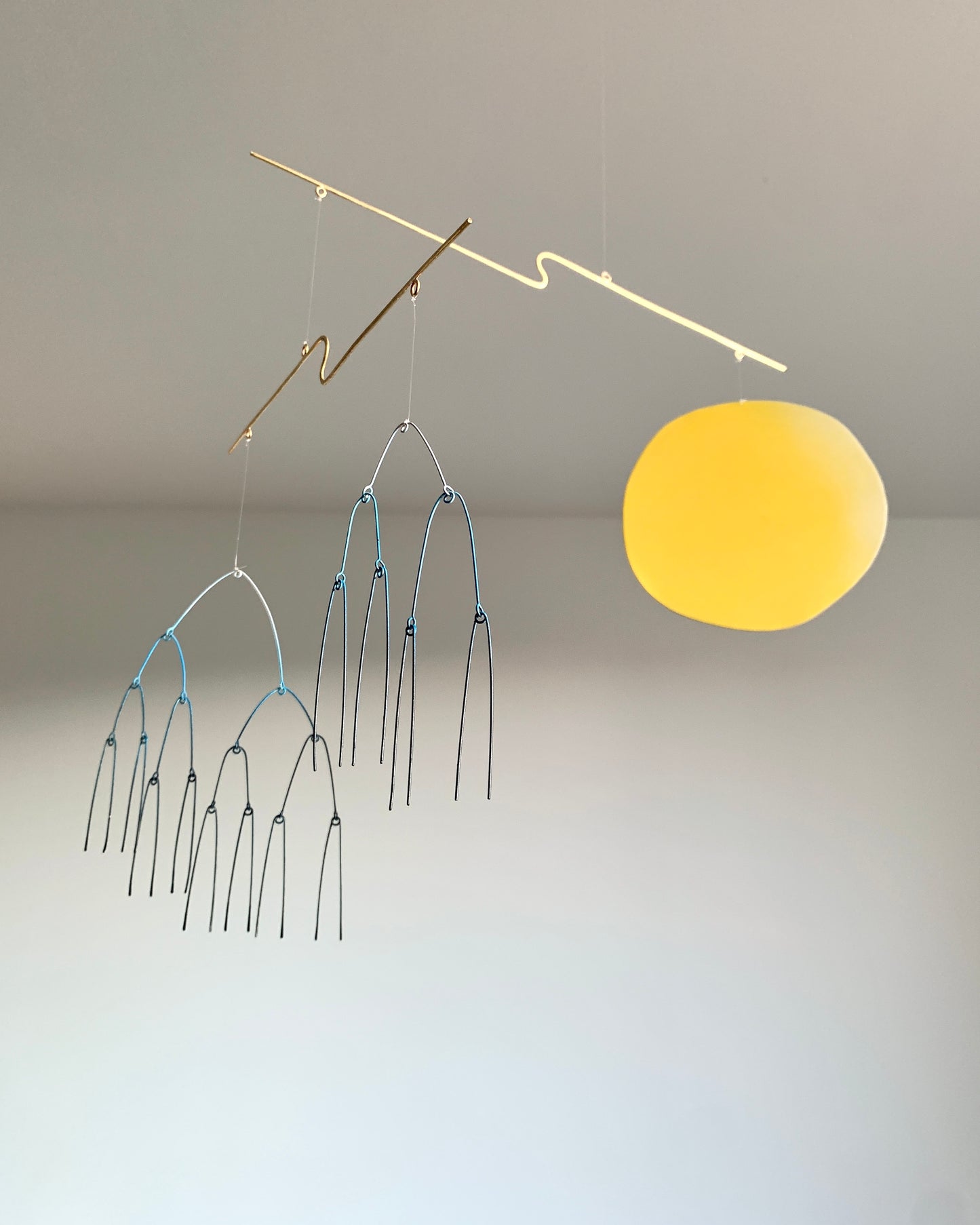 Decorative hanging mobile with a yellow circle and metal arches on a plain background