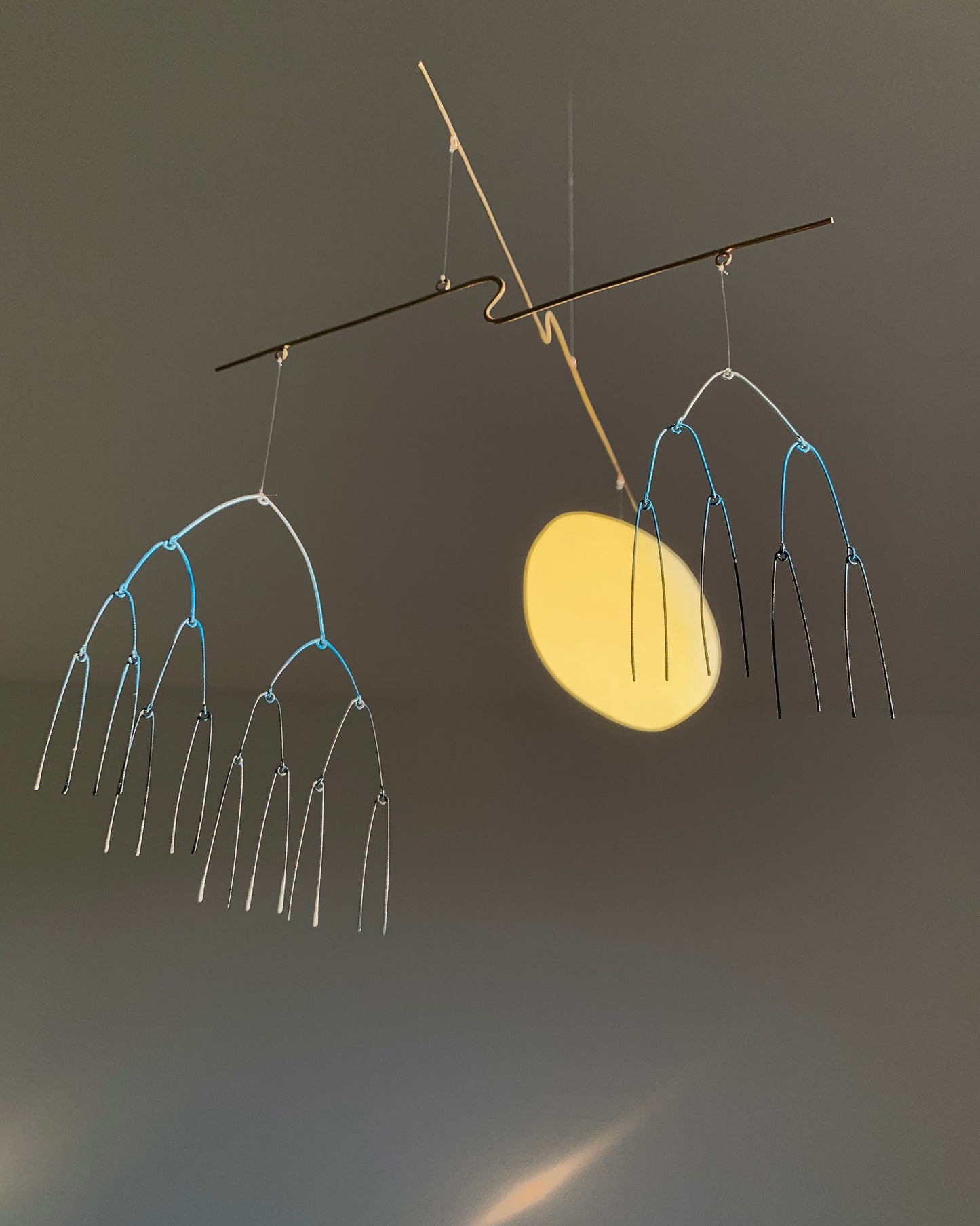 Abstract metal sculpture with hanging branches against a dark background