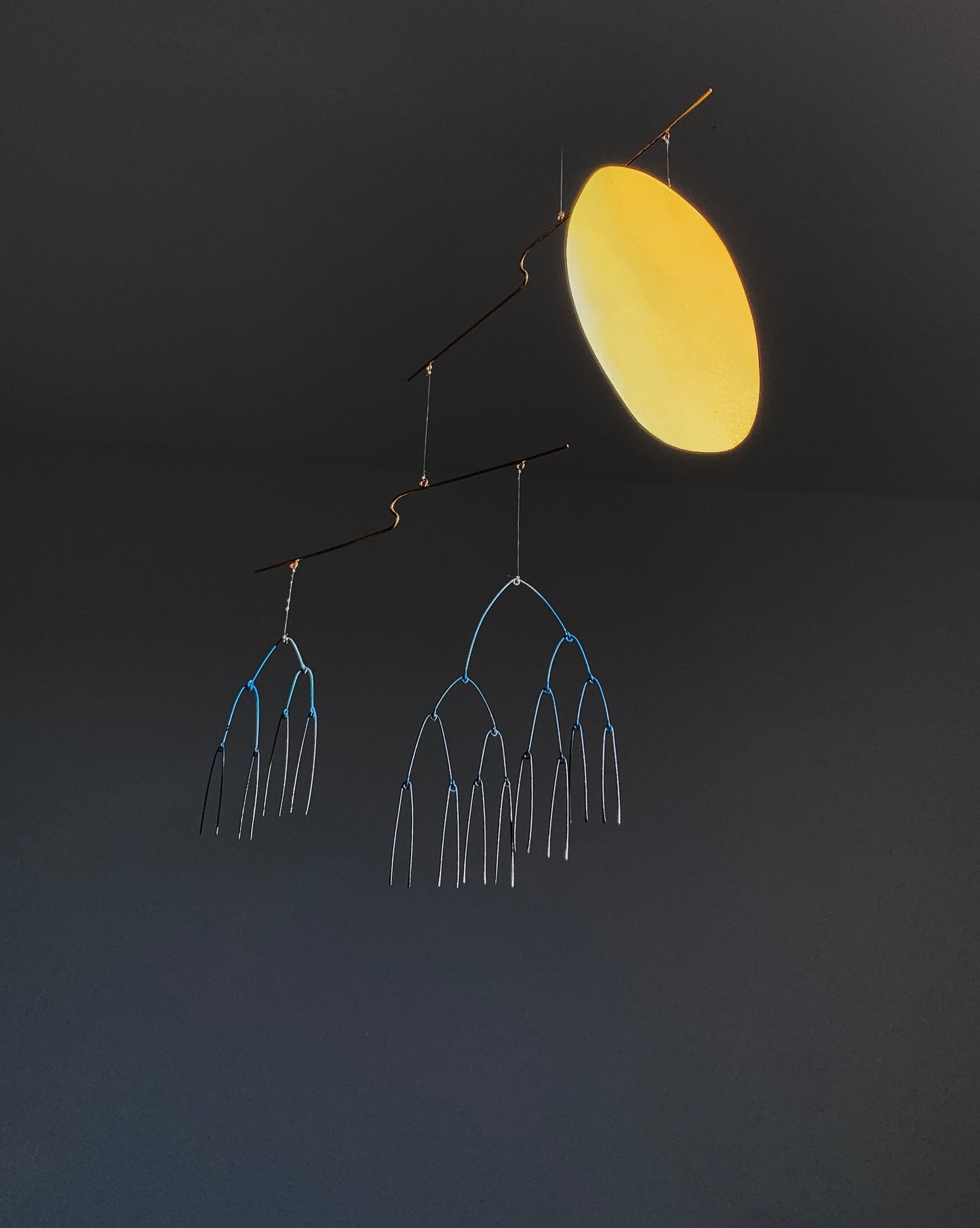 Sculpture with a yellow oval and metal branches on a dark background