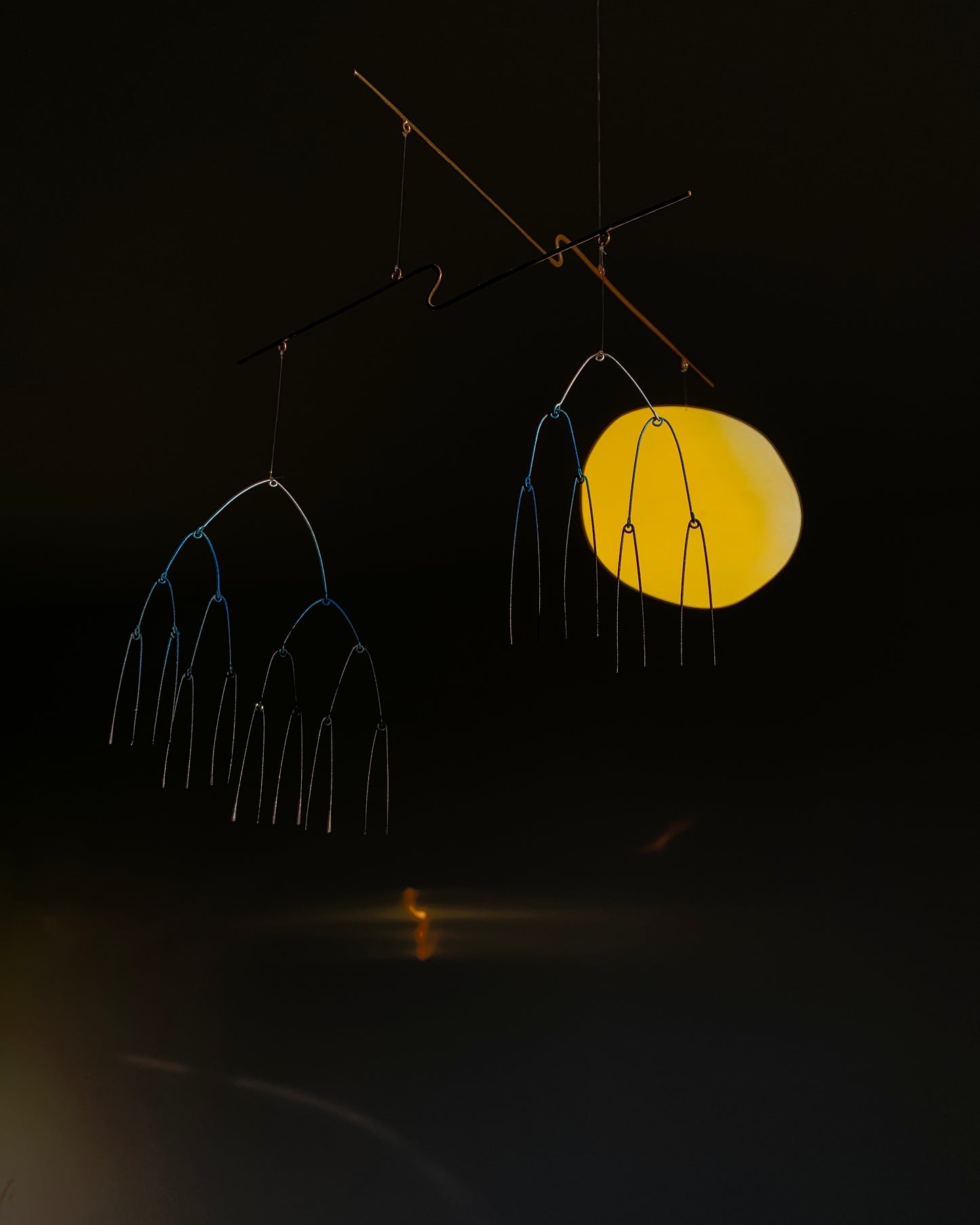 Hanging sculpture with a yellow circular piece against a dark background