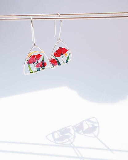 triangle shaped silver earrings with floral colorful design on a light gray background