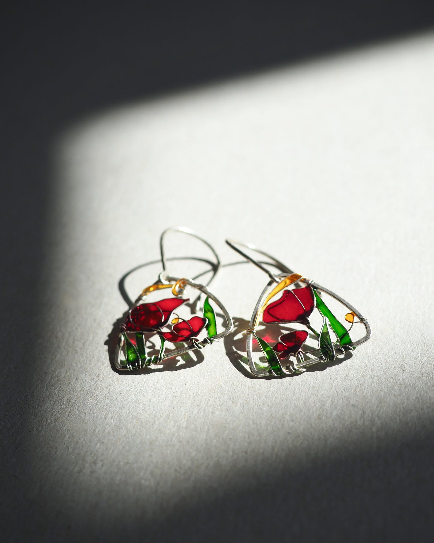 Pair of earrings with red poppy design on a light background