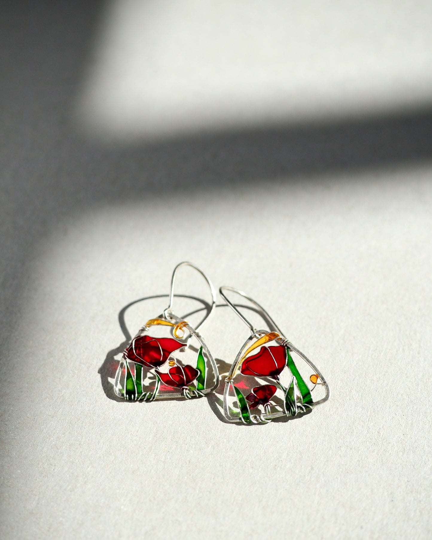 Triangle-shaped silver earrings with red and green design on a light gray background