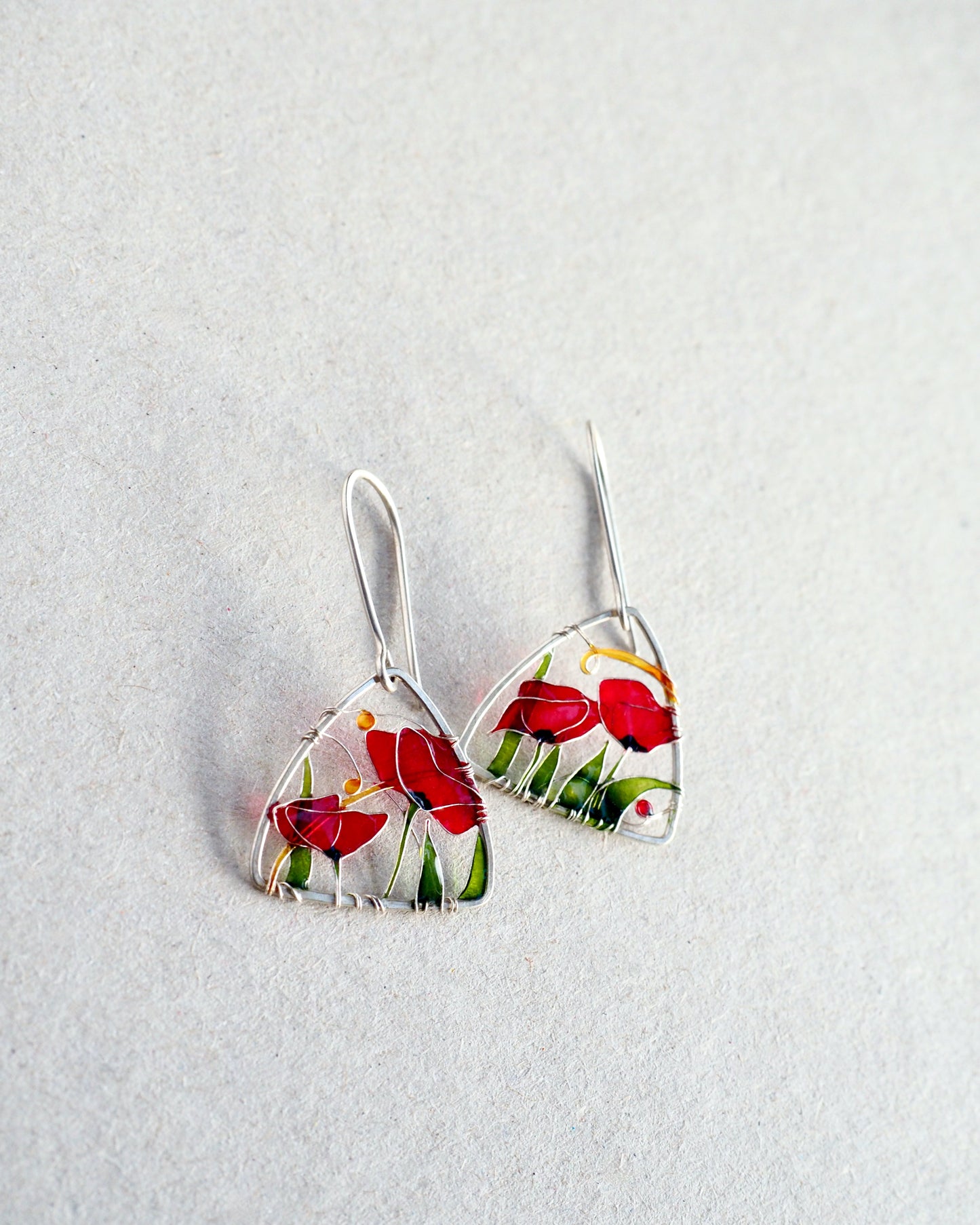 Triangle-shaped earrings with poppy floral design on a light gray background